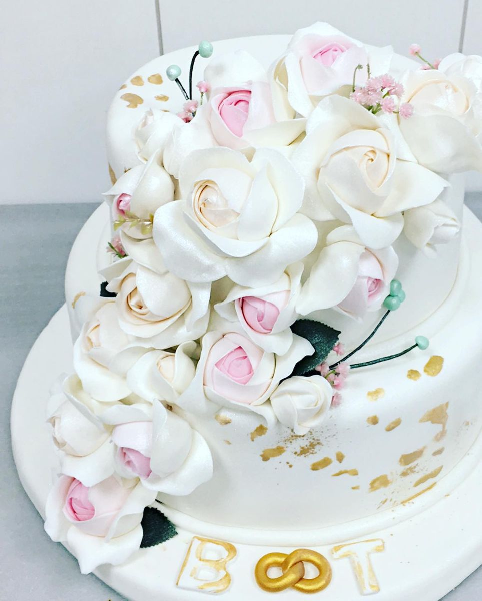 White wedding cake covered in handmade sugar roses with gold leaf accents